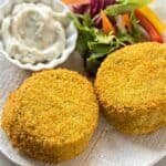 Crispy golden-brown vegetable patties served with a side of creamy dipping sauce and a fresh salad featuring colorful vegetables.