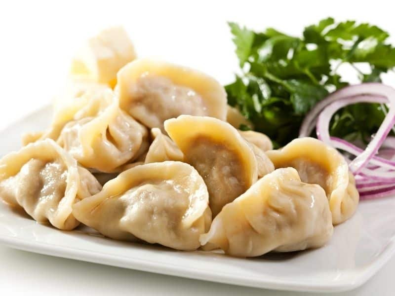 Plate of freshly steamed dumplings served with cilantro and dipping sauce, showcasing a popular Asian dish.