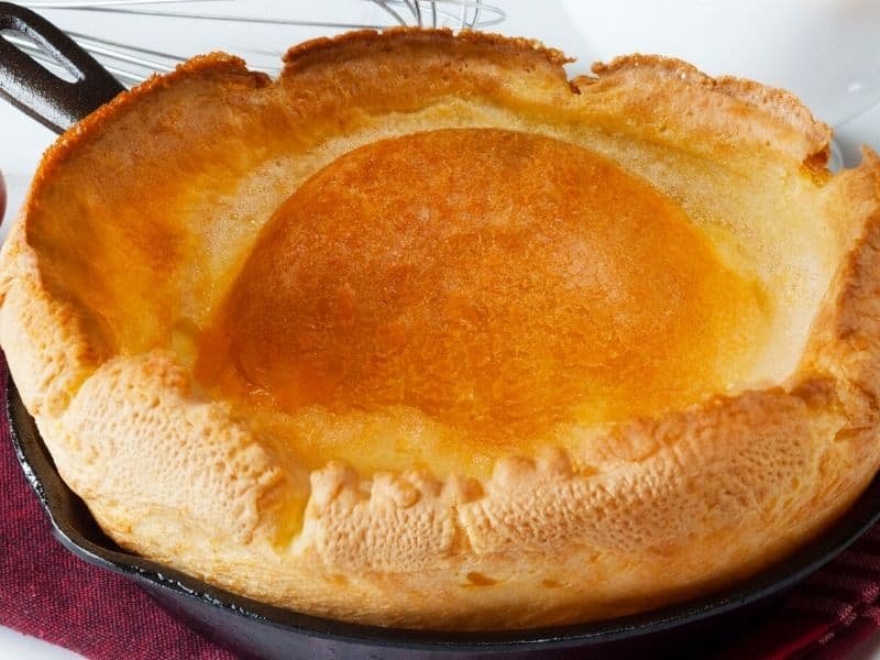 Golden brown Dutch baby pancake in a cast iron skillet, showcasing a fluffy, puffed texture and a smooth, round center.