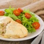 Savory chicken pastry served on a white plate with fresh green salad and cherry tomatoes, set on a rustic table.