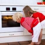 Two young children curiously peering into an oven in a bright kitchen, showcasing a family cooking experience.