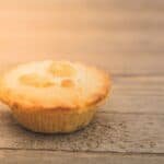 Golden-brown pastry pie on a wooden surface, showcasing a flaky crust and a creamy filling.