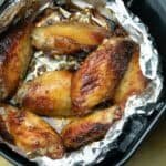 Crispy grilled chicken wings arranged on a bed of foil in a black serving dish, showcasing a golden-brown, charred exterior, ideal for a flavorful appetizer or party dish.