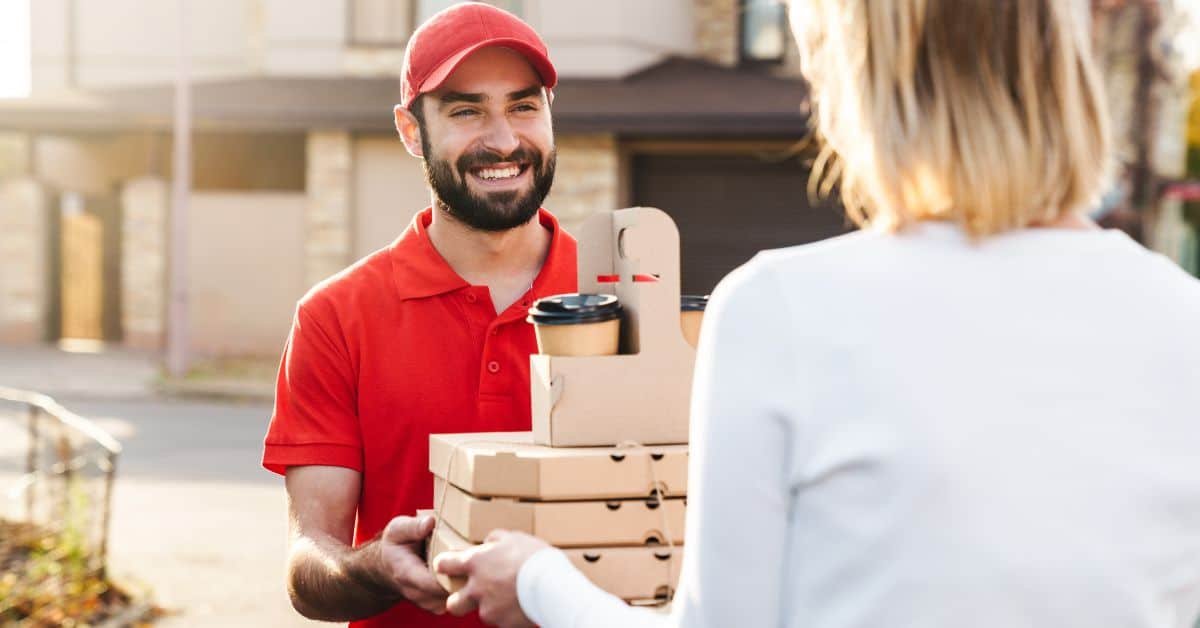 Delivery person handing over pizza boxes and coffee to a customer at home, showcasing a friendly interaction and efficient food delivery service.