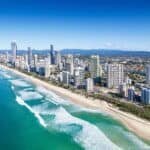 Aerial view of the Gold Coast skyline with sandy beaches and turquoise waters under a clear blue sky.