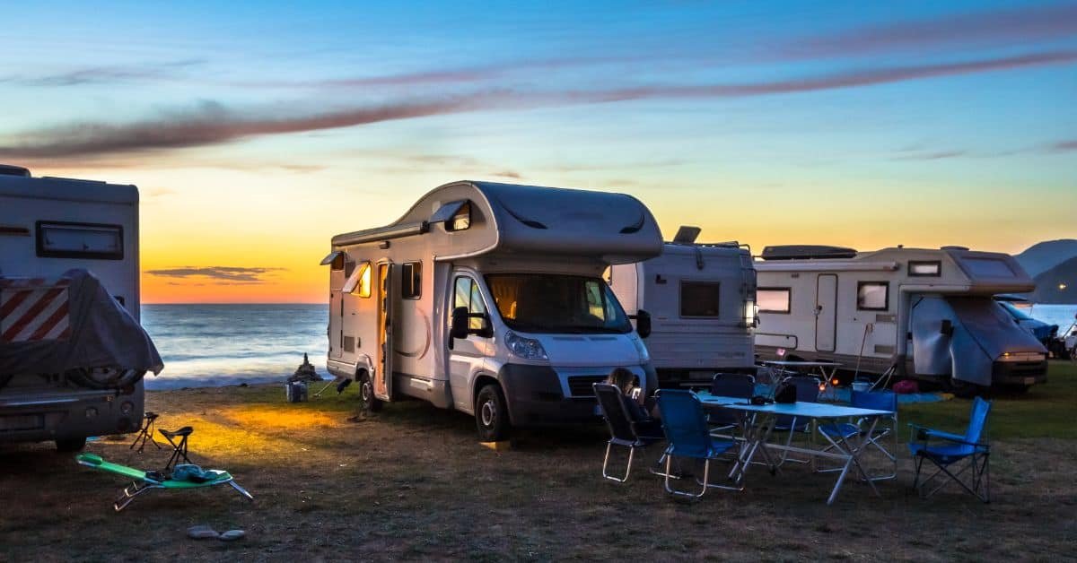 Motorhome parked by the beach at sunset, with camping chairs set up nearby, showcasing a peaceful outdoor camping experience.