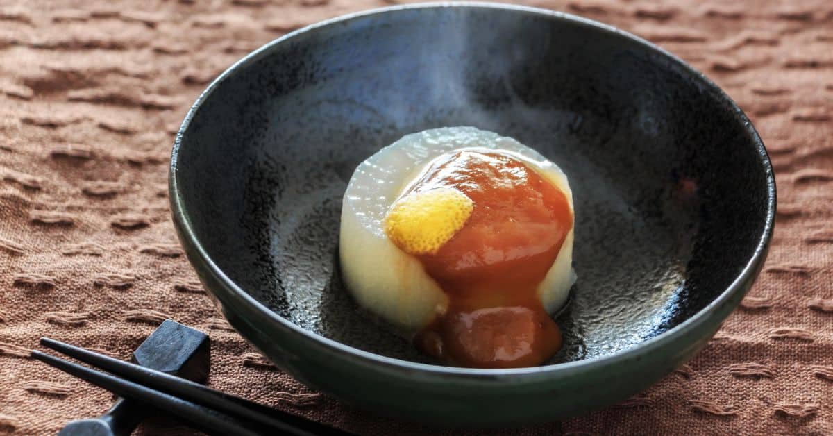 Steaming Japanese dessert served in a black bowl, featuring a soft, glutinous rice cake topped with a dollop of sweet syrup and a slice of butter.