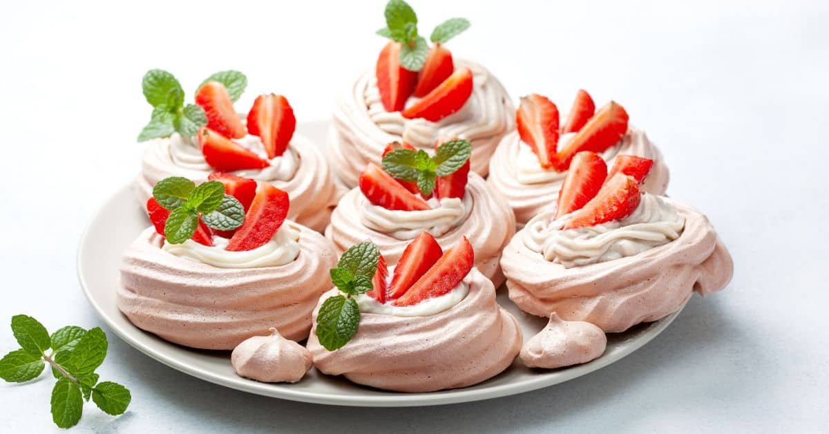 Delicious meringue desserts topped with fresh strawberries and mint leaves, arranged on a white plate. Perfect for a summer treat or special occasion.