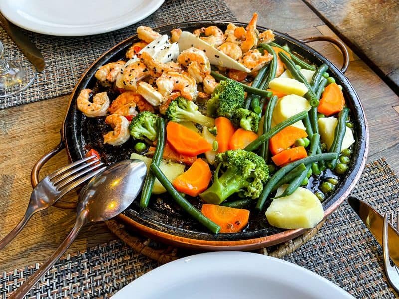 Grilled shrimp and mixed vegetables including broccoli, carrots, green beans, and potatoes served on a rustic platter, perfect for a healthy meal.