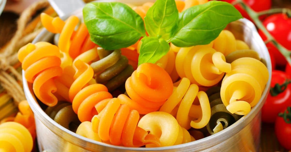 Colorful spiral pasta dish with orange, yellow, and green noodles garnished with fresh basil leaves. Perfect for a vibrant and healthy meal option.