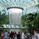 Indoor waterfall surrounded by lush greenery and visitors at Jewel Changi Airport, Singapore, showcasing the stunning architecture and natural beauty of the attraction.