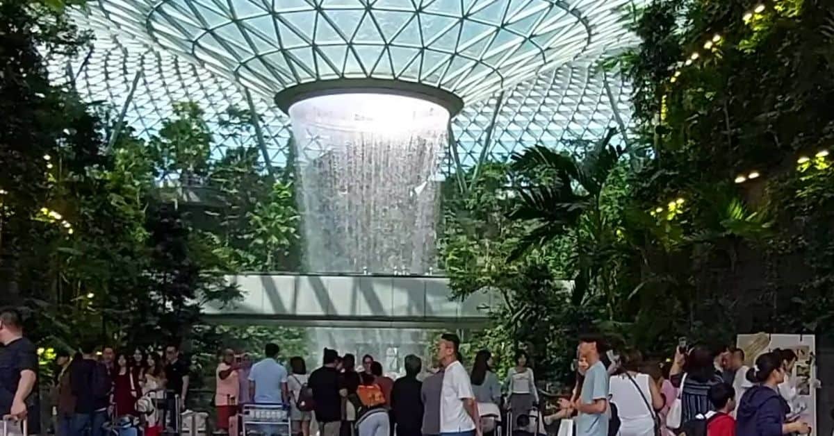 Indoor waterfall surrounded by lush greenery and visitors at Jewel Changi Airport, Singapore, showcasing the stunning architecture and natural beauty of the attraction.