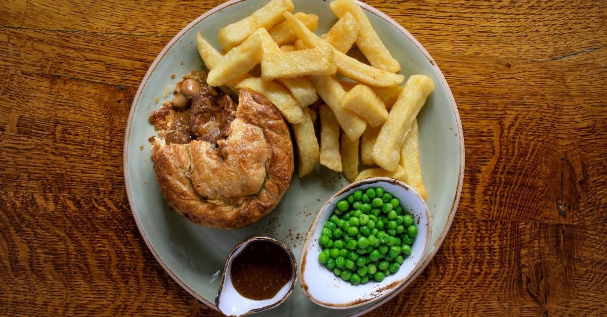 Plate of traditional British food featuring a meat pie, golden fries, and a side of green peas with gravy.