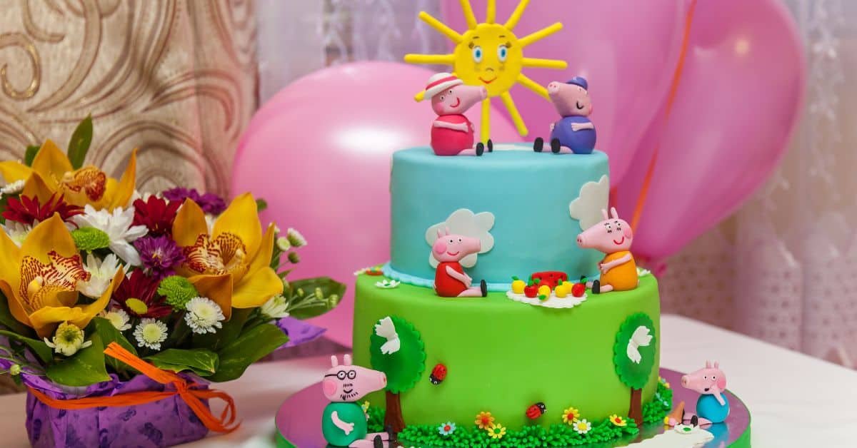 Colorful Peppa Pig themed birthday cake with playful decorations, including sun and cartoon characters, set against a festive background with balloons and flowers.