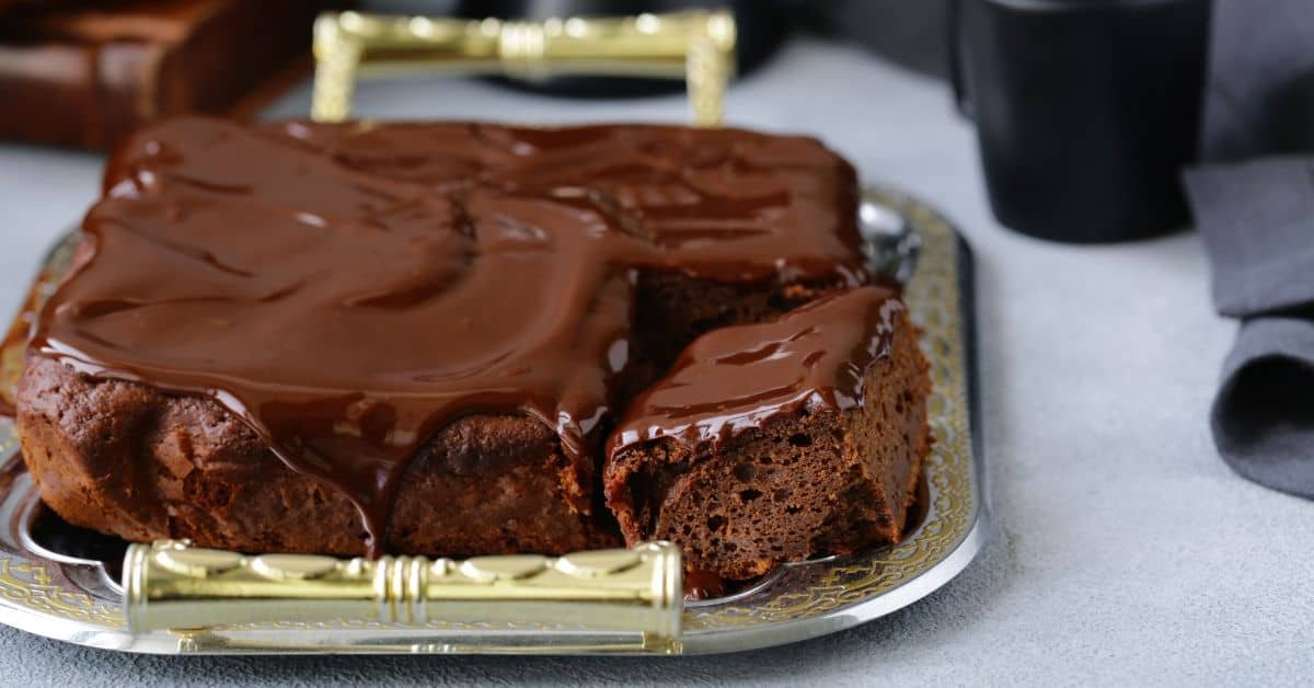 Decadent chocolate cake with a glossy ganache topping, served on a silver tray, showcasing rich textures and a moist interior. Perfect for dessert lovers and special occasions.