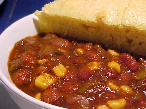 Bowl of hearty chili featuring beans, corn, and spices, served with a side of cornbread. Perfect for a comforting meal.