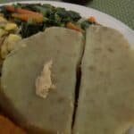 Plate of traditional food featuring a sliced portion of fufu alongside a colorful mix of sautéed vegetables, including carrots and leafy greens.