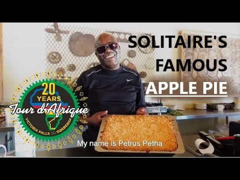 A smiling chef holding a freshly baked apple pie in a kitchen setting, celebrating 20 years of culinary expertise at Solitaire's Famous Apple Pie.