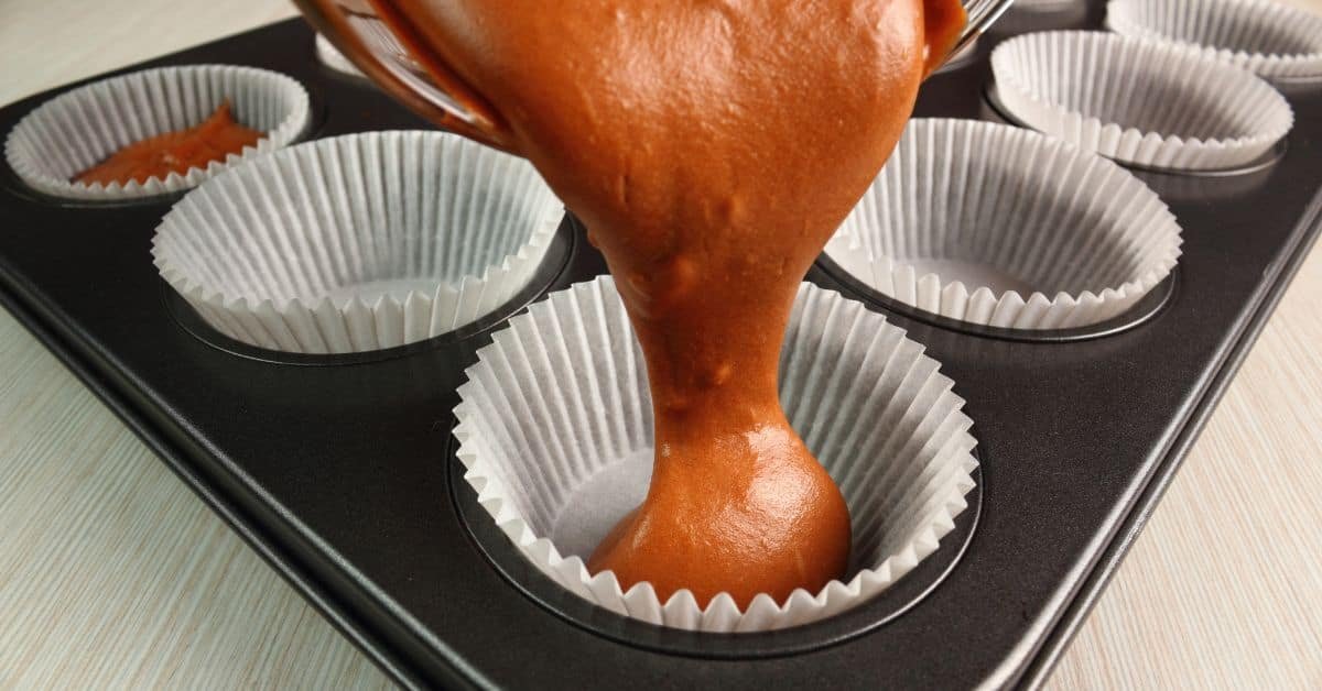 Chocolate batter being poured into cupcake liners in a muffin tray, ready for baking.