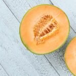 Halved cantaloupe melon on a light blue wooden surface, showcasing its orange flesh and seeds.