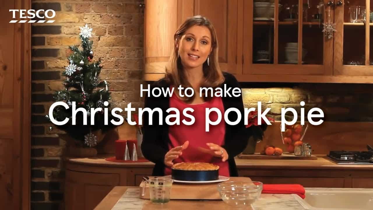 Woman demonstrating how to make Christmas pork pie in a cozy kitchen setting, with a Christmas tree in the background.