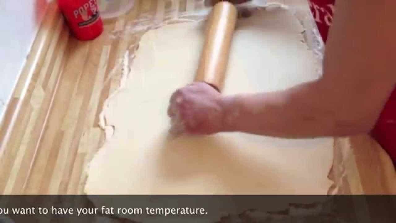 Person rolling out dough with a wooden rolling pin on a floured surface, demonstrating baking techniques for pastry preparation.