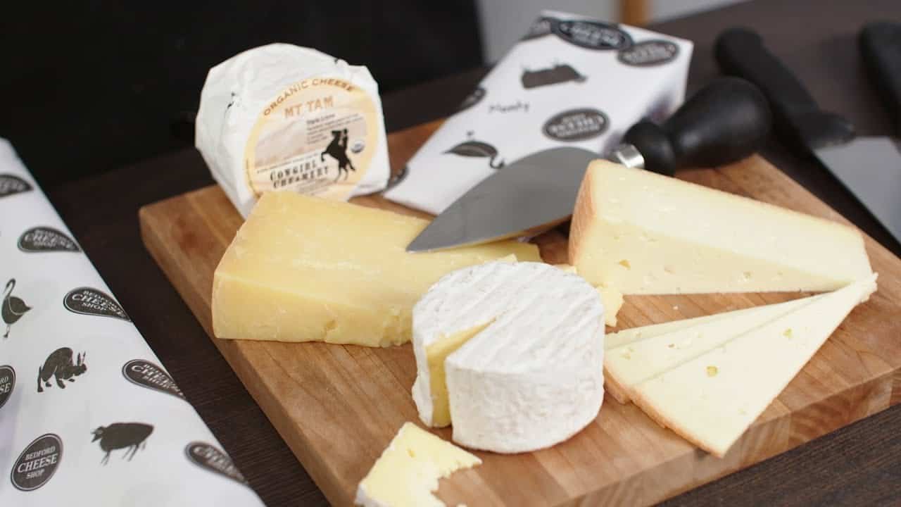 Assorted cheeses displayed on a wooden cutting board with a cheese knife, showcasing different textures and shapes, perfect for a cheese platter or tasting event.