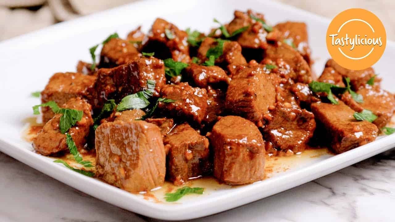 Tender chunks of marinated meat served on a white plate, garnished with fresh cilantro in a savory sauce, perfect for a delicious main course.