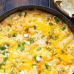 Baked cheesy dip with melted cheddar and green onions, served in a cast iron skillet, accompanied by tortilla chips. Perfect for parties and gatherings.