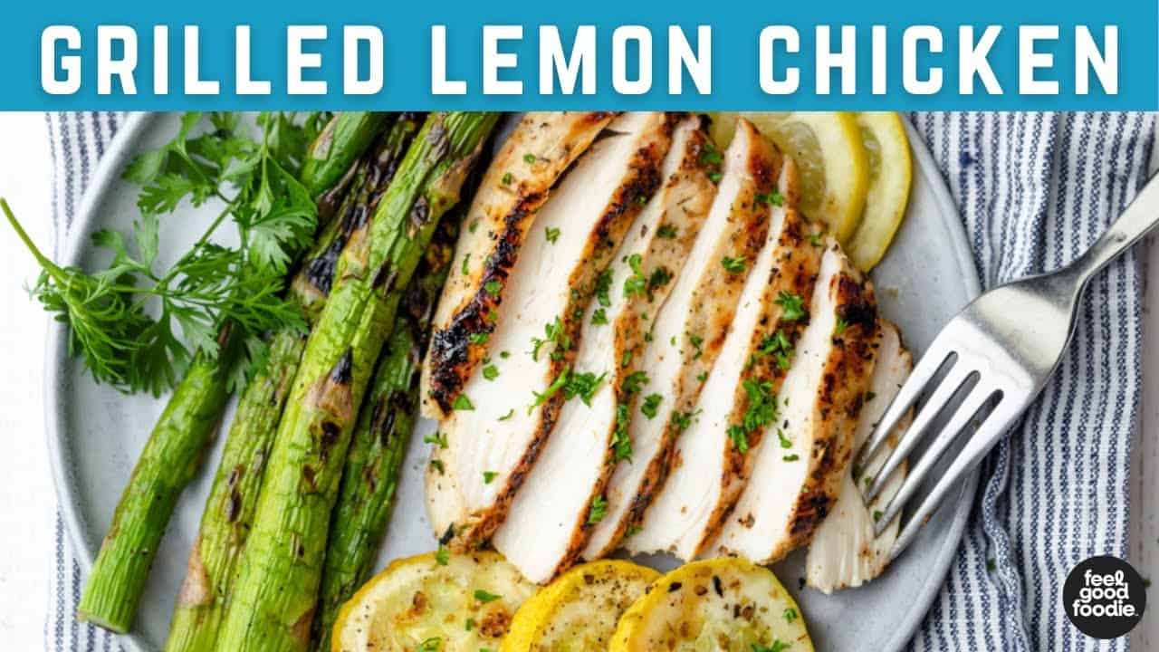 Grilled lemon chicken served with sliced lemon, grilled asparagus, and zucchini on a white plate, garnished with fresh herbs. Perfect for a healthy meal option.