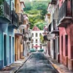 Colorful street view in a historic town with vibrant buildings and lush green hills in the background, showcasing a picturesque urban landscape.