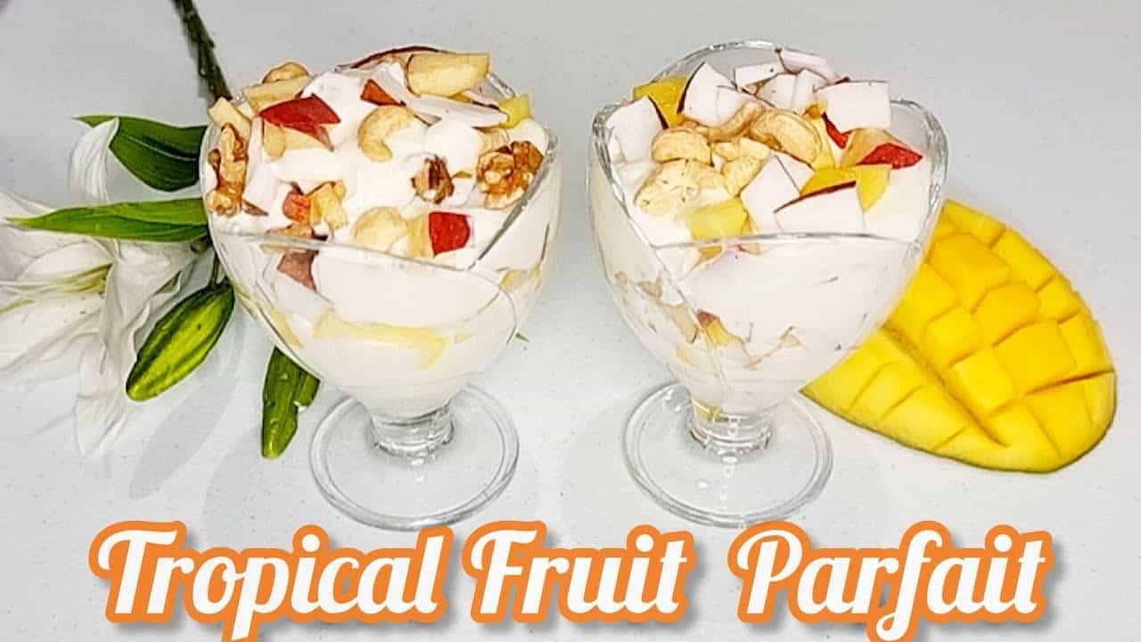 Two elegant glass bowls filled with tropical fruit parfaits, featuring layers of fresh fruits, creamy yogurt, and garnished with nuts. The parfaits are visually appealing, showcasing a variety of colors and textures, perfect for a refreshing dessert.