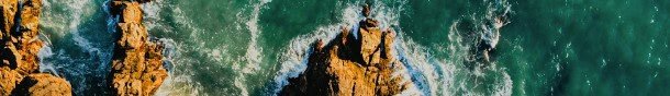 Aerial view of a rocky coastline with waves crashing against the shore, highlighting the contrast between the golden rocks and the turquoise ocean water.