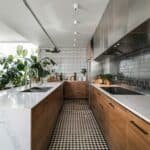 Modern kitchen design featuring sleek wooden cabinetry, marble countertops, and a patterned black and white tiled floor, complemented by abundant natural light and indoor plants.