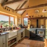 Bright and inviting rustic kitchen with yellow walls, wooden beams, and large windows showcasing a scenic view. Features include a farmhouse sink, wooden cabinetry, and a dual oven range, creating a warm and functional cooking space.