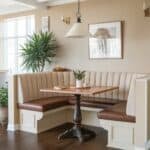 Cozy dining nook featuring a wooden table and upholstered seating, surrounded by natural light and decorative plants, ideal for a warm, inviting atmosphere.