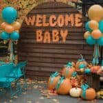 Colorful baby shower decoration featuring a wooden backdrop with "Welcome Baby" in orange letters, surrounded by teal and gold balloons and decorative pumpkins. The setup includes teal chairs and a festive autumn theme.