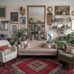 Cozy living room featuring a vintage sofa, green armchair, and an ornate rug, adorned with eclectic wall art and plants, creating a warm and inviting atmosphere.