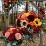 Vibrant autumn floral arrangements featuring sunflowers, dahlias, and roses, set against a rustic backdrop of trees, perfect for fall weddings or seasonal events.