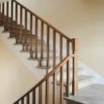 Interior staircase with wooden railing and light-colored walls, featuring stone steps and a modern design.