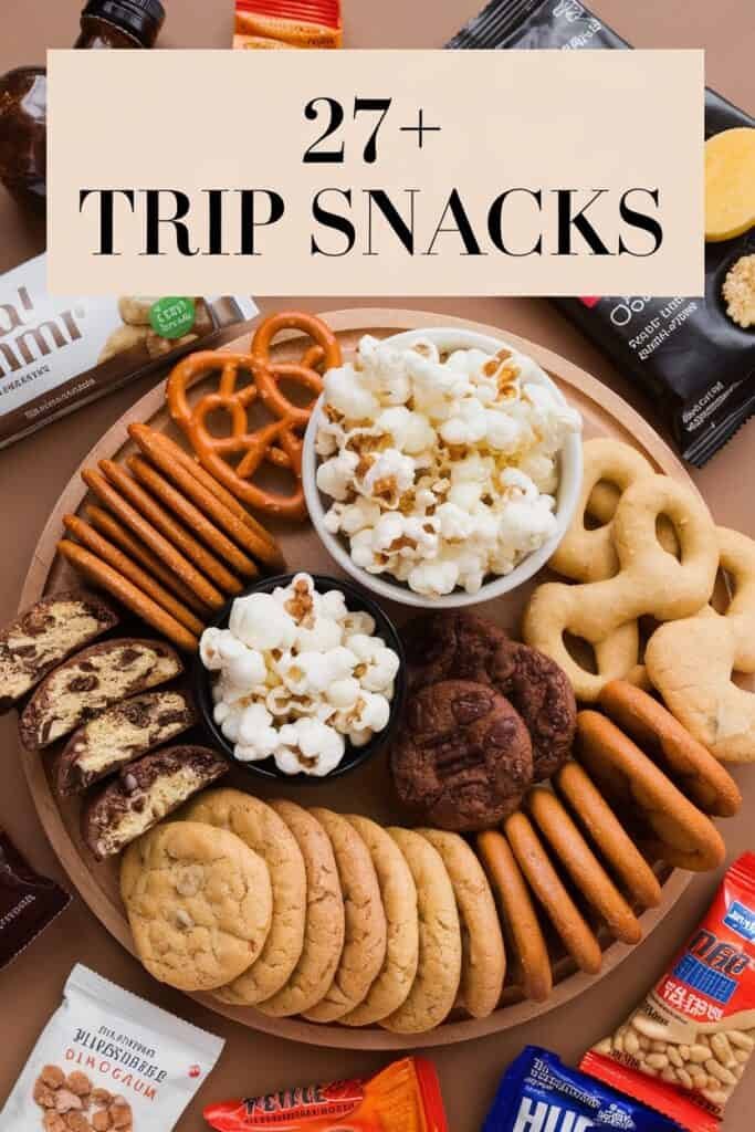 A variety of trip snacks arranged on a wooden platter, including popcorn, pretzels, cookies, and chocolate bars, showcasing over 27 snack options ideal for travel.