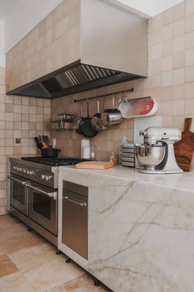 Modern kitchen featuring stainless steel appliances, marble countertops, and hanging cookware. The space includes a gas stove, a stand mixer, and a wooden cutting board, creating an inviting and functional cooking environment.