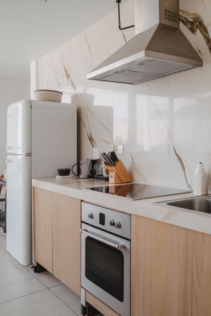 Modern kitchen featuring a white refrigerator, stainless steel oven, and a sleek marble backsplash. The wooden cabinetry complements the contemporary design, while kitchen utensils are neatly arranged on the countertop.
