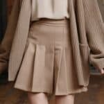 Woman wearing a stylish beige pleated skirt paired with a cozy oversized cardigan, showcasing a trendy fall outfit.