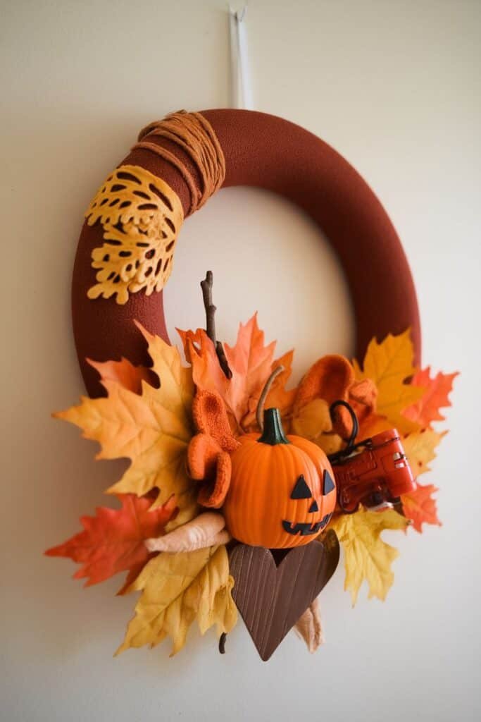 Autumn-themed wreath featuring a brown foam base adorned with artificial orange and yellow leaves, a small carved pumpkin, a wooden heart, and a vintage red toy tractor, perfect for seasonal home decor.