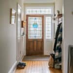 Welcoming hallway with a wooden front door featuring stained glass, light-colored walls, hardwood flooring, and a coat rack.