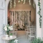 Elegant wedding ceremony setup featuring floral decorations, chiavari chairs, and a beautifully arranged backdrop with greenery and soft lighting.