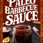 Jar of paleo barbecue sauce with a dark, rich color, accompanied by a slice of lemon and herbs, set against a dark background. The image promotes a collection of over 27 paleo barbecue sauce recipes.