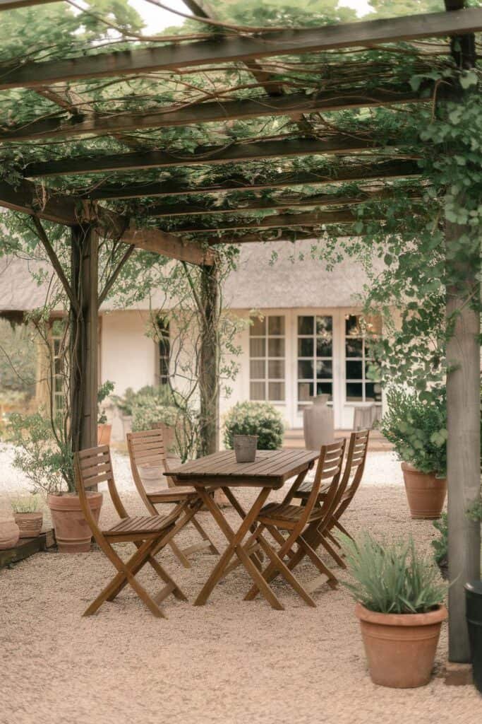 Outdoor dining area featuring a wooden table and chairs under a leafy pergola, surrounded by potted plants and a cozy, inviting atmosphere. Ideal for alfresco meals and relaxation in a garden setting.